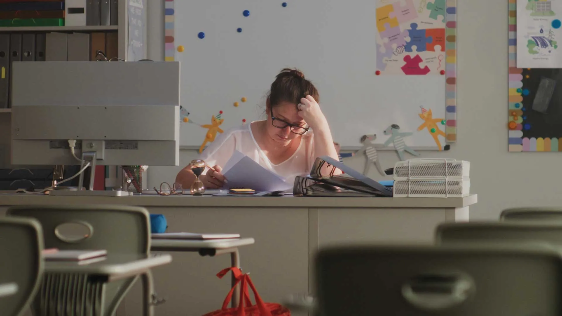 White female classroom teacher with her hand on her head in a dark classroom.