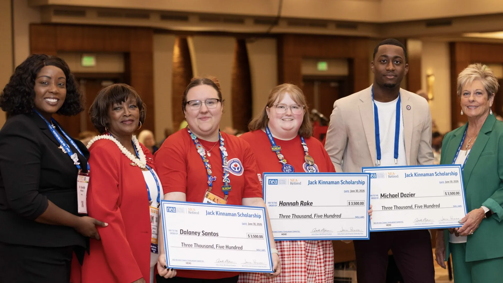 Six people pose for a picture, with 3 of the people holding oversized checks. 