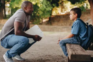male counselor stoops down to talk to an upset child on a bench outdoors