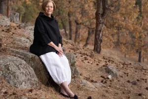 A woman seated on a rock surrounded by trees and natural greenery.