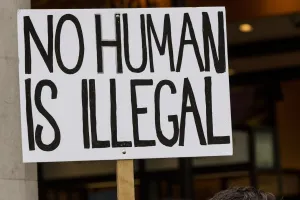 Rally sign that reads No Human is Illegal in black letters against a white background.