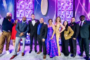 A group of people in formal attire stand on state to pose for a group picture