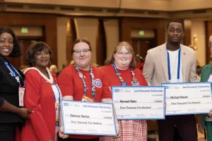 Six people pose for a picture, with 3 of the people holding oversized checks. 