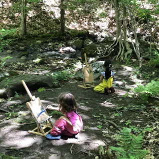 Photo of preschoolers at painting easels in woods