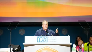 David Edwards, the general secretary of Education International addresses NEA delegates from a lectern addresses RA delegates