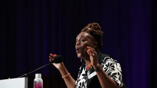 Terese Hodge sings at the lectern as part of her 2025 speech to the NEA RA