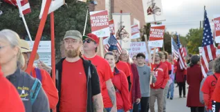 Educators and supporters, many wearing red and holding signs, walk the picket line.