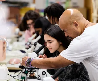 A male science teacher A man and student examine a sample through a microscope.