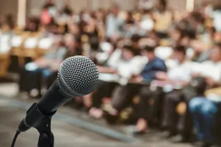 An empty microphone stands in front of a waiting audience