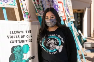 New Mexico educator stands in front of signs asking for respect for educator voices.
