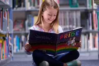 young girl in the library reading a copy of The Night Before Pride