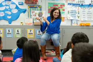 Teacher holds up book in front a class of students.
