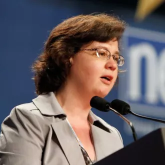NEA General Counsel Alice O'Brien stands at a podium in front of a microphone.