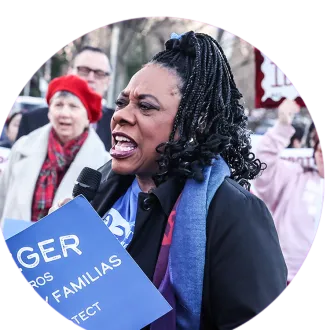 Becky Pringle addresses a crowd outside and holds a blue sign