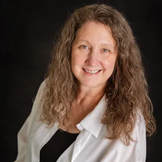 A woman with long curly hair smiles while posing in front of a black backdrop. 