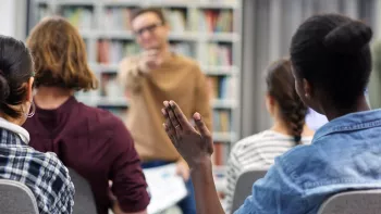view of students in class from behind one girl raises her hand