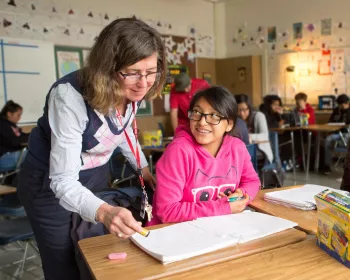 Smiling educator helps a student with her classwork. 