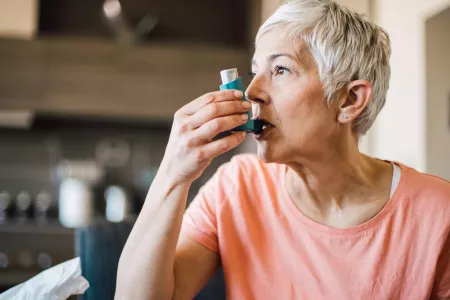A middle-aged woman uses an asthma inhaler