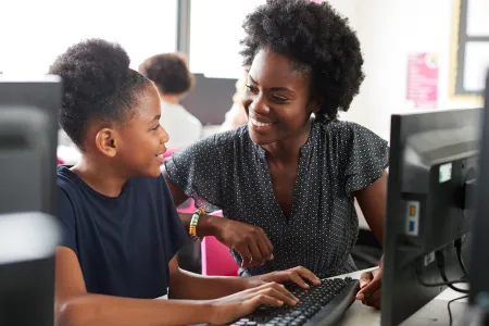 Black teacher and student work together in school computer lab
