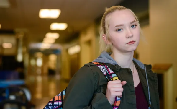 Teen girl in a school hallway with a serious expression.
