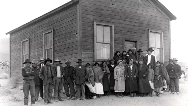 A black and white 1920s photo showing a large group of people in front of a log building.