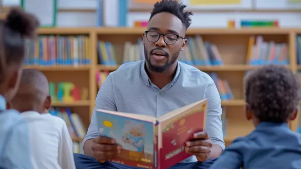 Black male teachers reads aloud to young children in a library