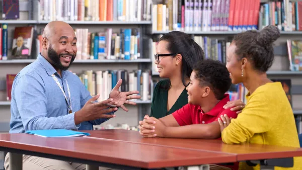 Parents, students and teacher sit at table and have a discussion