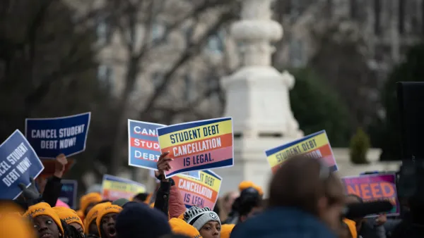 Activists holding signs about cancelling student debt stand together at a rally.