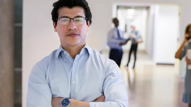 An Asian American male teacher poses in a school hallway