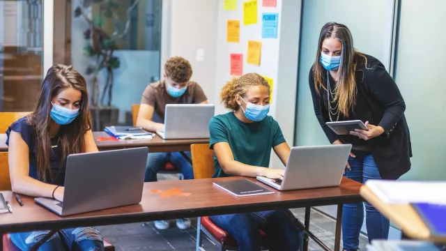 A teacher helps students use laptop computers