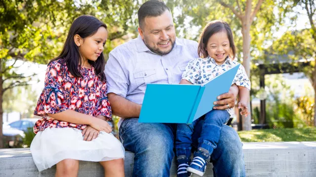 A father reads to his two daughters outside