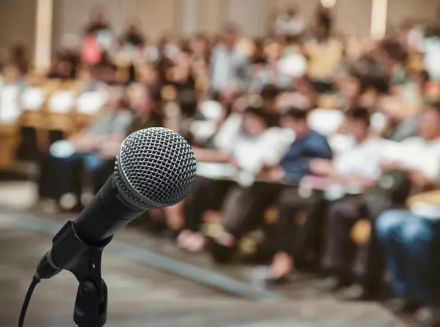 An empty microphone stands in front of a waiting audience