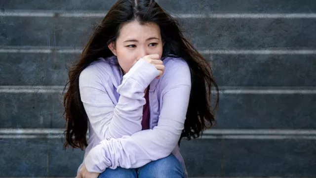 upset Asian girl student sitting on school steps