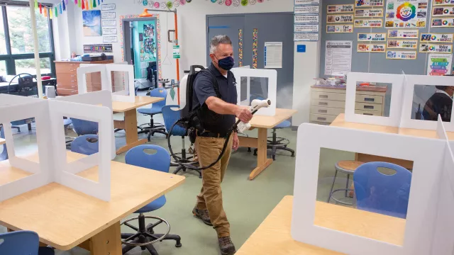 A member of the janitorial team sprays disinfectant to clean a classroom at Middletown High School.