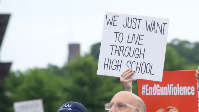 person at a rally holding a sign at a rally that reads "We just want to live through high school"
