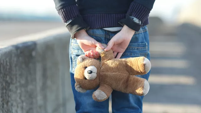 child holding teddy bear behind their back and walking away