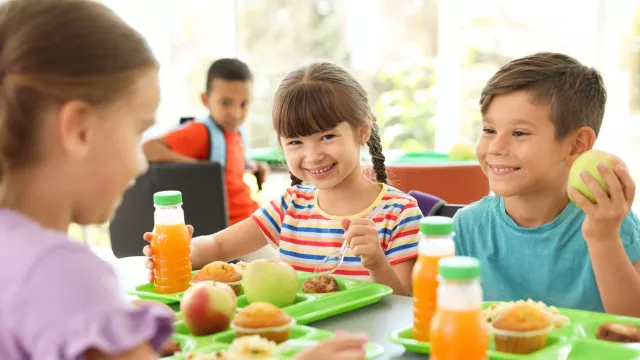 A group of students smiles and eats lunch in a school cafeteria