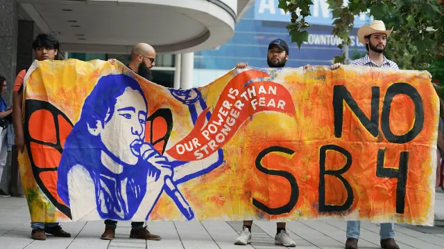 Activists hold orange protest sign that says No SB4