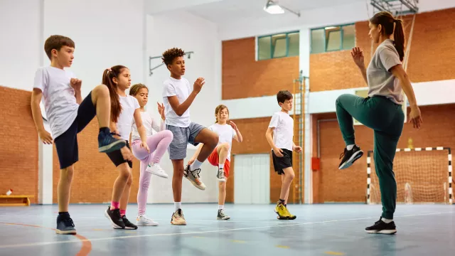 Six students exercise led by a teacher in PE class