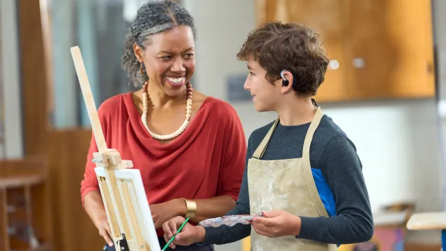 An art teacher works with a student at an easel