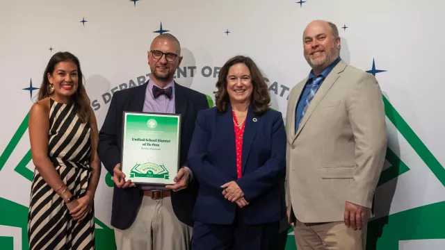 Four representatives from the Unified School District of De Pere holding up their Green Ribbon Award Plaque