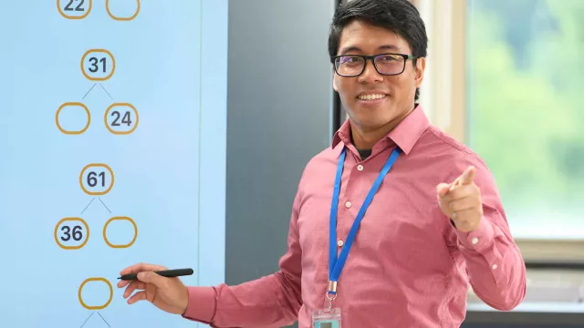 An male Asian teacher writes on a whiteboard