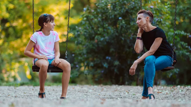 Mother and daughter sit on swings in the park and talk