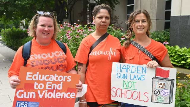 three educators wear orange and carry signs to protest gun violence