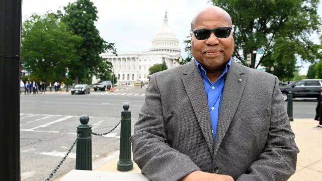 NEA-Retired member in suit and sunglasses poses in front of the US Capitol building