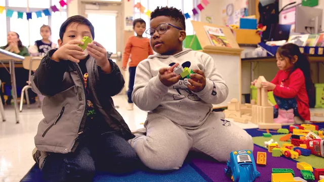 Two boys play with blocks on a rug in a preschool classroom