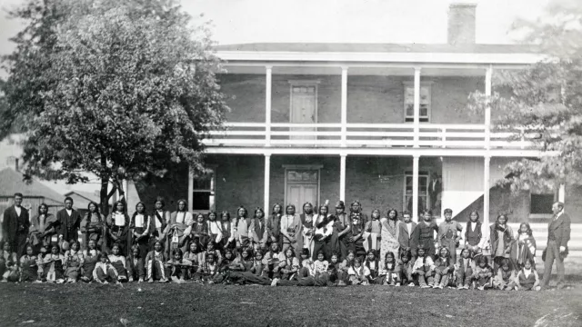 Sioux Boys standing and seated for a group photo in front of Carlisle Training School sometime between 1876-96