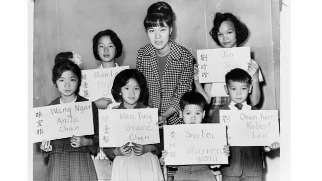 Six Chinese American students and their teacher hold up signs with their names in their native language and English
