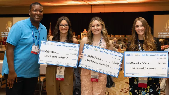 four college students hold up oversized scholarship checks at the NEA Retired Annual Meeting