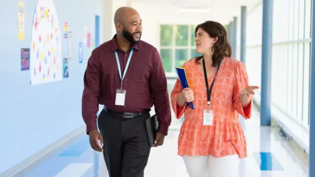 two teachers talk while walking down a school hallway